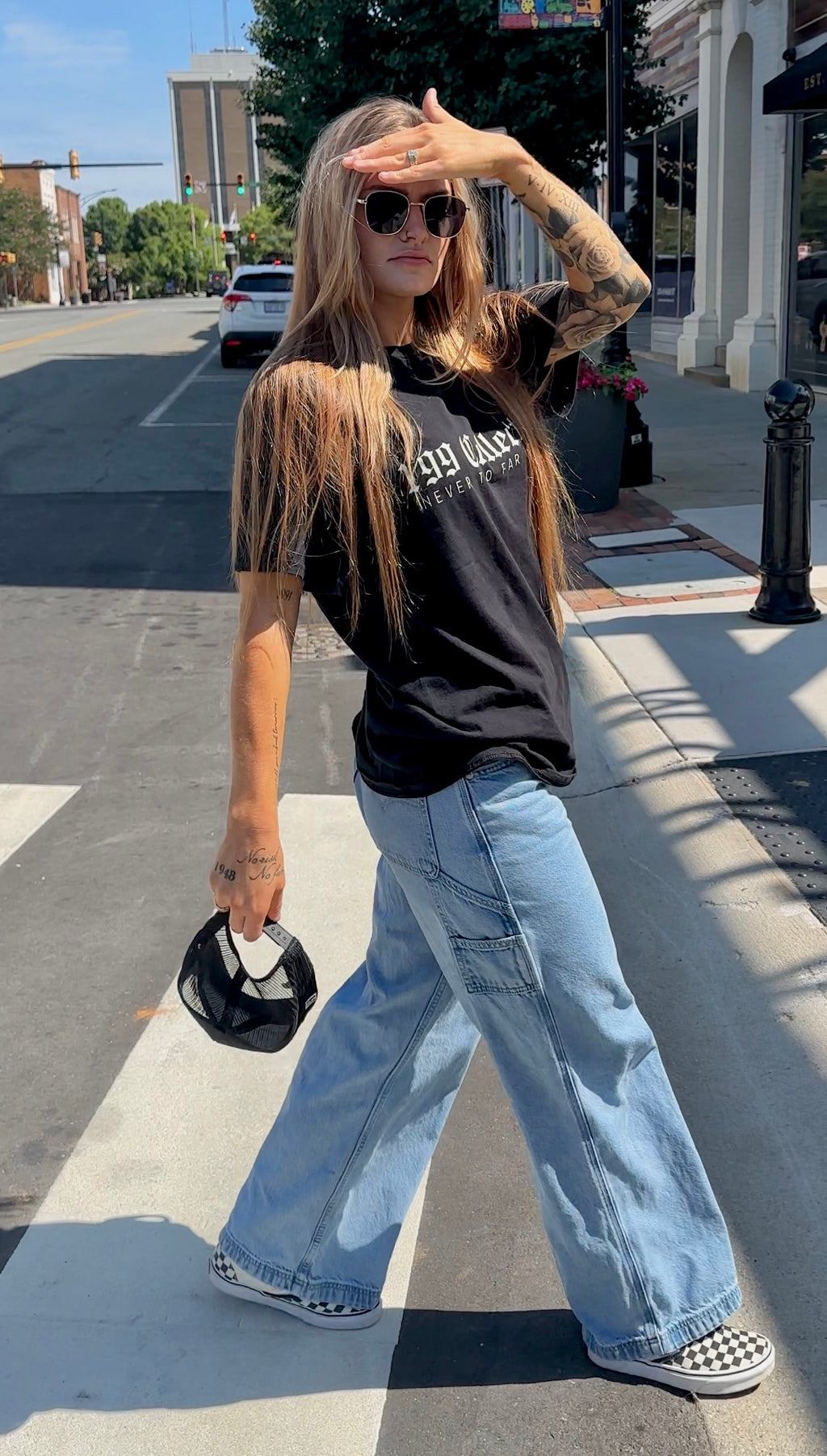 Person wearing a black t-shirt with text and light blue jeans on a city street.